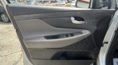 Close-up of a car's interior door panel with armrest, chrome door handle, and window controls; parking lot seen through the window and side mirror in the background.