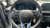 Driver’s perspective of the car interior with a leather steering wheel, instrument cluster, and an infotainment screen; parked cars visible through the windshield.