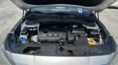 Open car hood revealing engine bay and visible battery on the right in a parking lot.