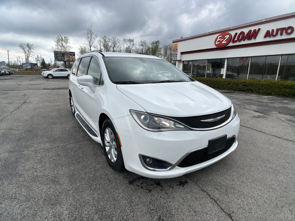 White minivan parked in the foreground outside an EZ Loan Auto building on a cloudy day in a dealership lot