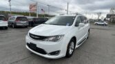 White Chrysler minivan in the foreground at a used-car lot with an EZ Loan Auto Sales sign and an American flag under a cloudy sky.