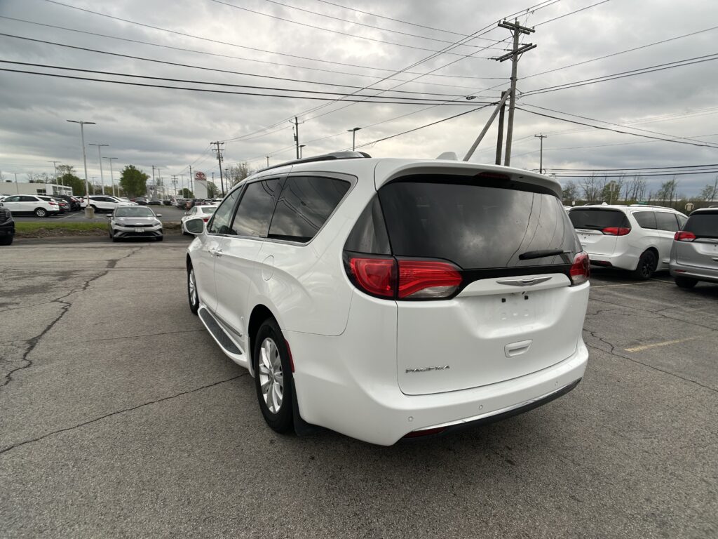 Rear-right view of a white Chrysler Pacifica in a crowded parking lot, with tall power lines overhead and a cloudy sky behind.