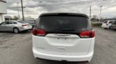 Rear view of a white Chrysler Pacifica minivan in a parking lot with other cars and a cloudy sky behind it.