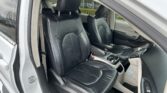 Front interior of a car with black leather seats and orange contrast stitching, center console and steering wheel visible.