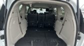 Open rear hatch of a white minivan showing a spacious cargo area with folded third-row seats and black flooring; front seats visible ahead.