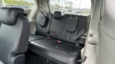 Interior of a black leather SUV with third-row seating and headrests; dealership lot visible through the rear window.