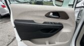 Interior of a car door: beige panel with brown trim, window controls, and a silver door handle; side mirror visible outside the window; parking lot in background.