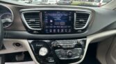 Interior of a car dashboard with a large touchscreen display in the center and gear shifter below, view of a parking lot outside through the windshield