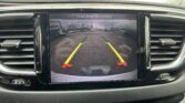 Car rearview camera screen showing a parking lot with yellow guide lines and the text 'Check Entire Surroundings' at the top, during reverse.