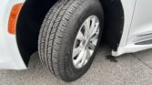 Close-up of a tire mounted on a white vehicle, showing the tread pattern and orange side marker on the fender.