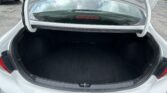 Open trunk of a silver sedan viewed from above, showing an empty black cargo area and the car's rear windshield with a red brake light centered in the glass.