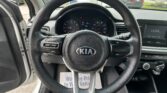 Interior view of a Kia from the driver’s seat, showing the steering wheel, dashboard gauges, and center console with exterior parked cars visible through the windshield.