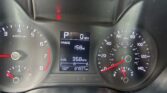Car dashboard with speedometer and tachometer, central digital readout showing range and average MPG, warning light illuminated above.