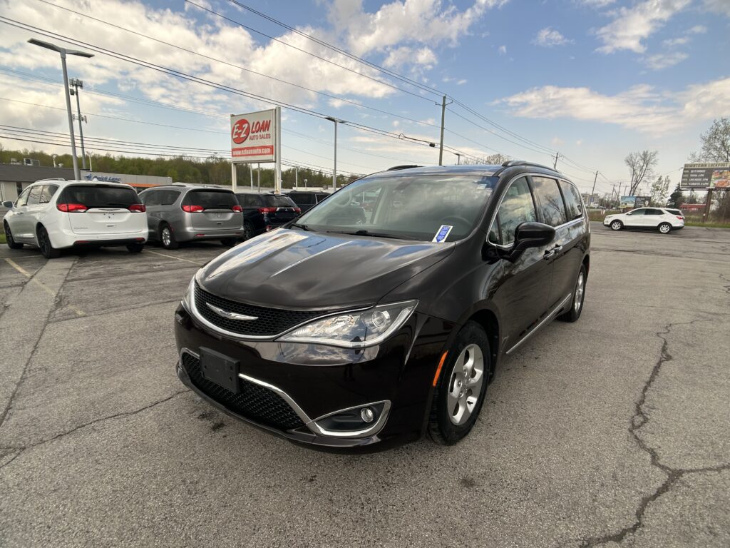 Black minivan in foreground at a car dealership lot with other vans, sign reading 'EZ Loan Auto Sales' and power lines in the sky