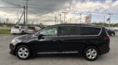 Black minivan in a dealership lot with other cars, power lines overhead, and a cloudy sky in the background.
