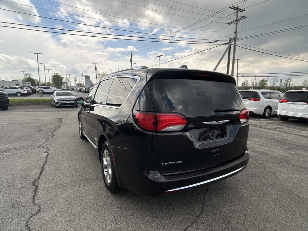 Rear three-quarter view of a black Chrysler Pacifica SUV in a car dealership lot with other vehicles and power lines overhead.