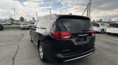 Rear three-quarter view of a black Chrysler Pacifica SUV in a car dealership lot with other vehicles and power lines overhead.