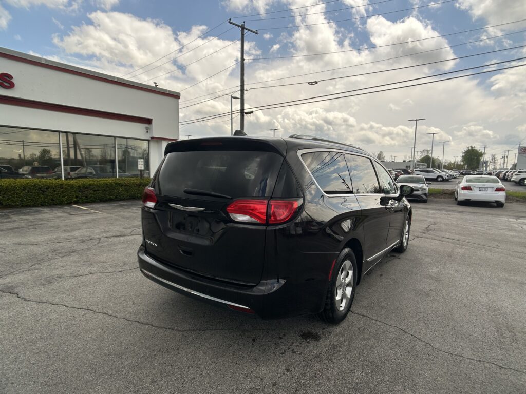 Black SUV parked in a car dealership lot with a white building on the left and rows of cars in the background under a cloudy sky, daytime.