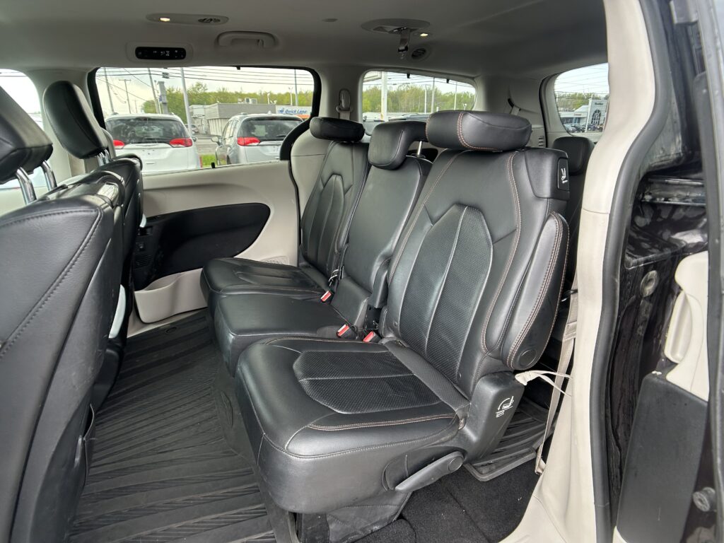 Black leather three-row vehicle interior with captain chairs and rear seating, visible parking lot outside through the windows