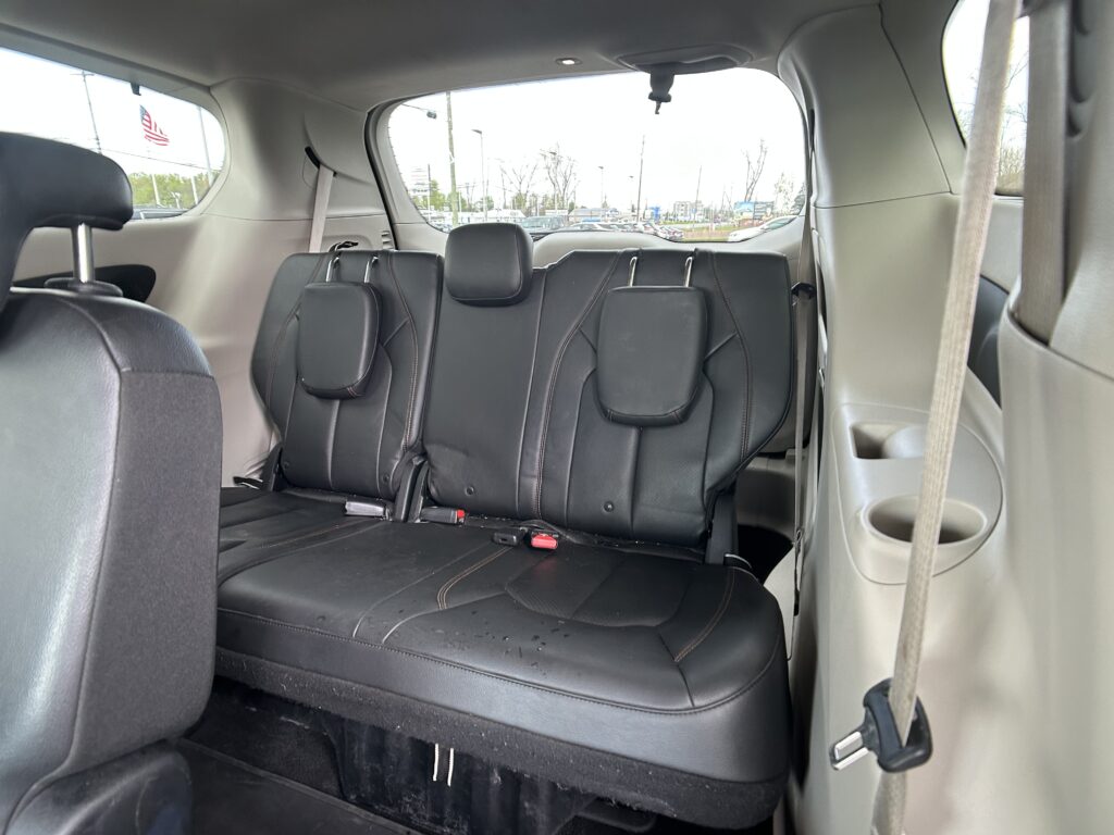 Interior of a gray SUV showing black leather rear seats with headrests and a parking-lot view through the windows. The second row is upright with visible seat belts.