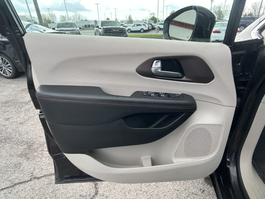 Interior of a car door panel: light gray textured surface with a silver door handle and black armrest containing window controls at the bottom center.