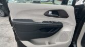 Interior of a car door panel: light gray textured surface with a silver door handle and black armrest containing window controls at the bottom center.