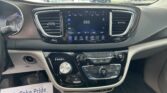 Center console infotainment screen displaying 550 AM radio with climate and control icons, surrounded by the car’s dashboard and vents. Outside through the windshield is a busy dealership lot.