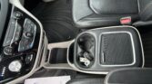 View of a car's center console and front seats, showing climate control panel, cup holders, and a red seatbelt buckle beside the leather seat.