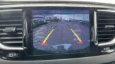 In-dash rearview camera display showing parking guide lines and the street behind the car; text 'Check Entire Surroundings' appears on screen.