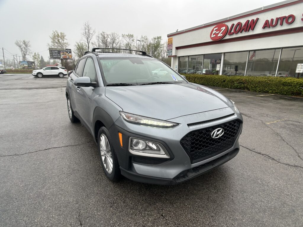 Gray Hyundai SUV in a rainy parking lot in front of an EZ Loan Auto dealership building with large glass windows and red signage.
