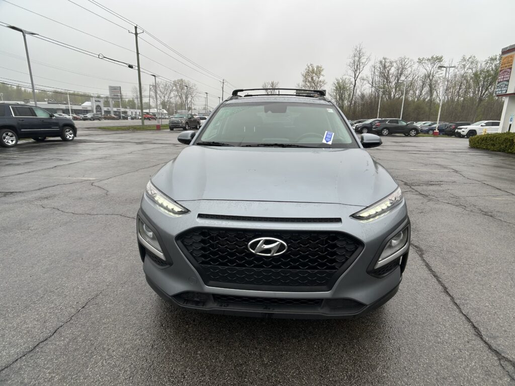 Front view of a gray Hyundai SUV with a roof rack, parked in a rainy dealership lot.