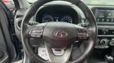 Driver's view of a car interior with steering wheel, instrument cluster, and center touchscreen on a rainy day outside the windshield.