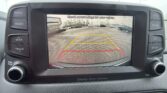 In-car display showing a rear-view camera view with parking guidelines and a warning to check surroundings for safety.