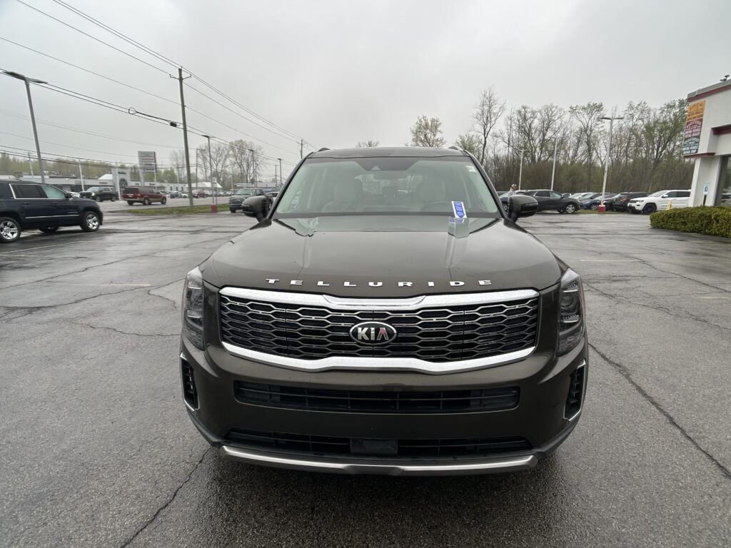 Front view of a black Kia Telluride SUV in a dealership parking lot on a cloudy day.
