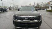 Front view of a black Kia Telluride SUV in a dealership parking lot on a cloudy day.