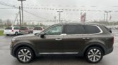 Close-up of a dark gray SUV parked in a car lot with other minivans in the background and power lines overhead.