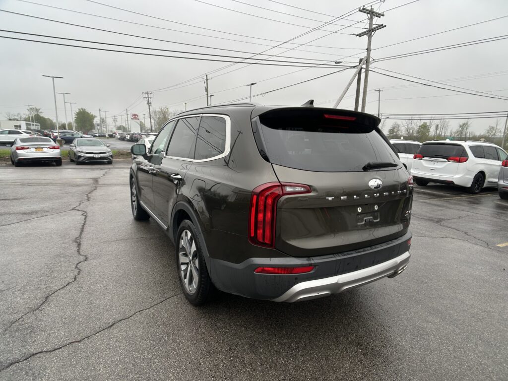 Rear view of a dark gray Kia Telluride in a dealership lot, with other cars and overhead power lines.