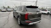 Rear view of a dark gray Kia Telluride in a dealership lot, with other cars and overhead power lines.