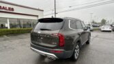 Rear three-quarter view of a gray Cadillac SUV (SV6) in a dealership parking lot, with a white building and 'SALES' sign in the background.