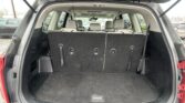 Open hatch of an SUV showing a large cargo area with the third-row seats folded down, revealing a flat black carpet and roomy trunk space.