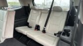 Interior of a car’s back seat with three beige leather seats and visible seat belts