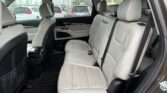 Rear passenger seating in a SUV with light gray leather seats and three headrests; window shows a parking lot with white cars outside.