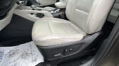 Front interior of a car: light beige leather driver and passenger seats, center console with gear shifter, and paper floor mat dirty with mud stains on the dark carpeted floor.