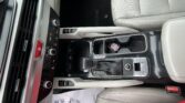 Interior of a car showing the center console with gear shifter, climate controls, and cup holders; beige seats and a paper on the floor with keys in the cup holder