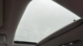 Interior of a car with the sunroof open, showing a gray sky through the glass panel.