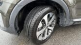 Close-up of a car's front wheel well showing a tire with an alloy rim and wet mud around the fender.