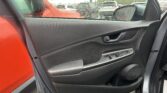 Interior of a car door panel with a rain-speckled window looking out onto a crowded parking lot.