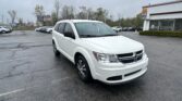 White SUV in the foreground of a wet parking lot, with a dealership building on the right and other cars in the background on a cloudy day.