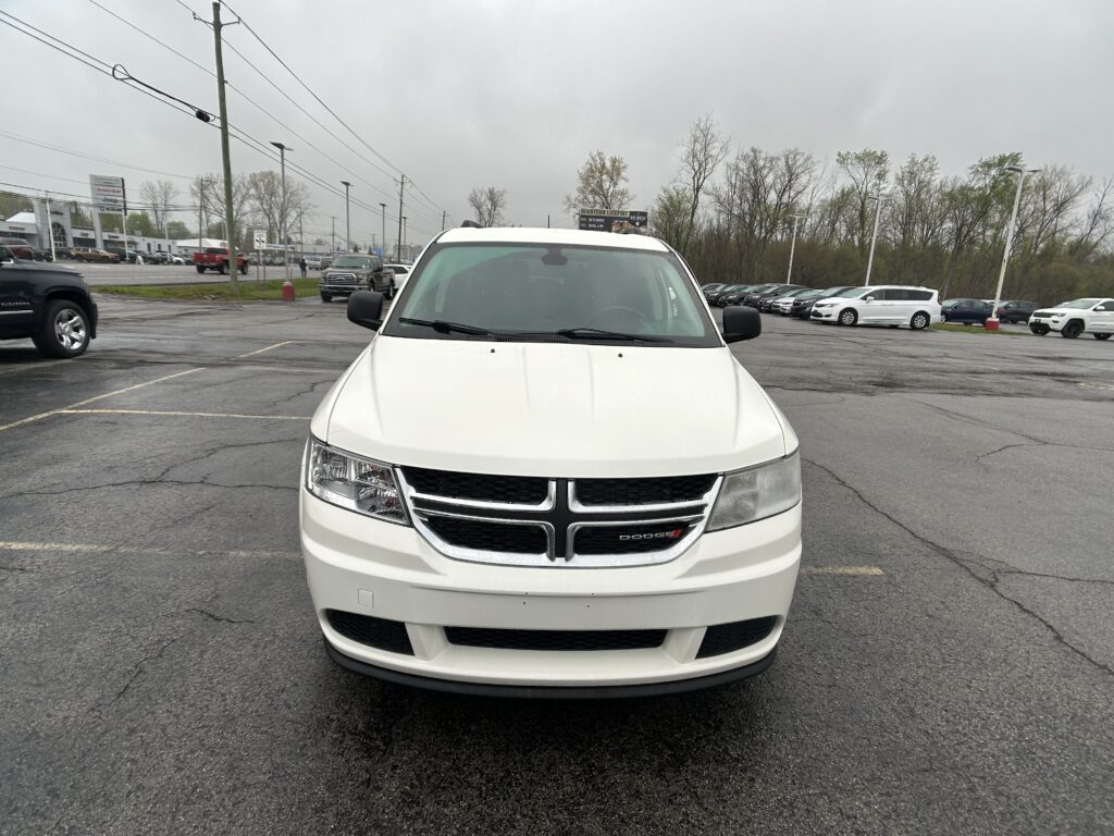 White Dodge SUV photographed from the front in a dealership lot on a cloudy day, with other cars and a building in the background, level with the hood.