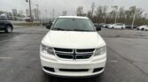 White Dodge SUV photographed from the front in a dealership lot on a cloudy day, with other cars and a building in the background, level with the hood.